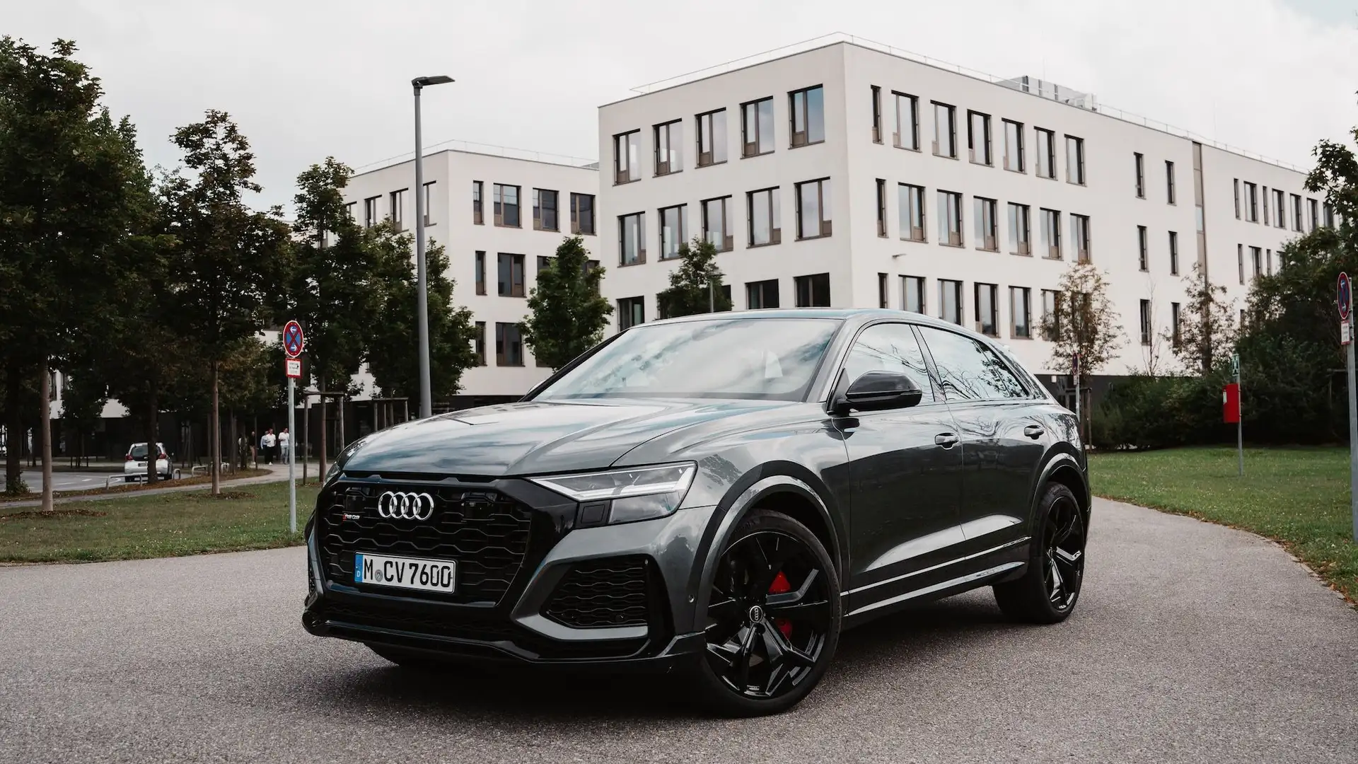 Unser grauer Audi RS Q8 auf einer begrünten Nebenstraße von vorne links fotografiert.